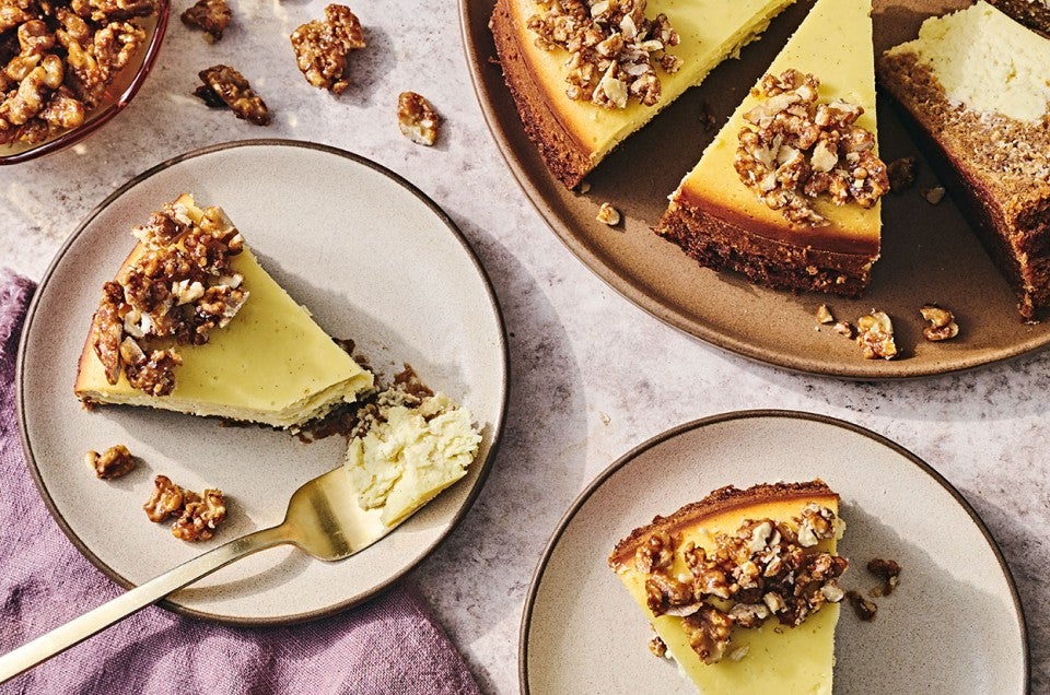 Carrot Cake Cheesecake on a table with slices on plates showing a golden cheesecake rimmed with nuts. - select to zoom