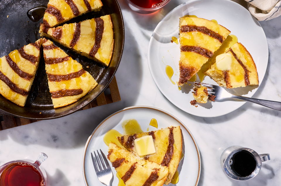A Cinnamon Roll Skillet Pancake sliced up and shown in a cast iron skillet and also on plates. - select to zoom