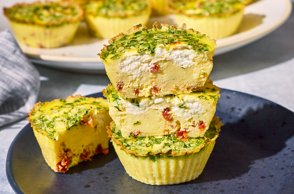 Egg Bites stacked on a plate with a cross-section showing a quiche like interior with greens, cottage cheese, and red pepper. - select to zoom