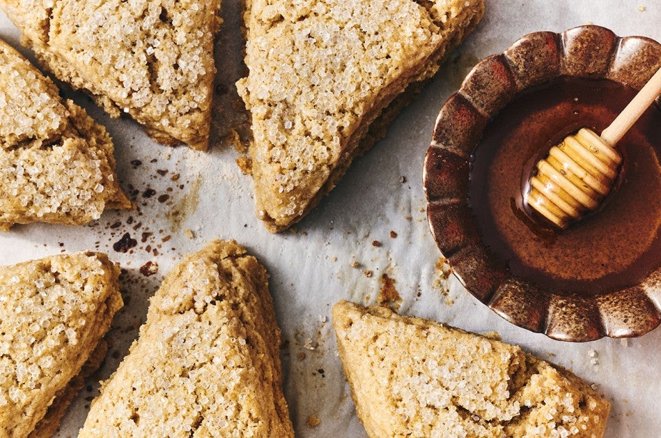 Looking down on Golden Wheat Scones with coarse sugar on top of them and a bowl of honey with a wooden honey wand. - select to zoom