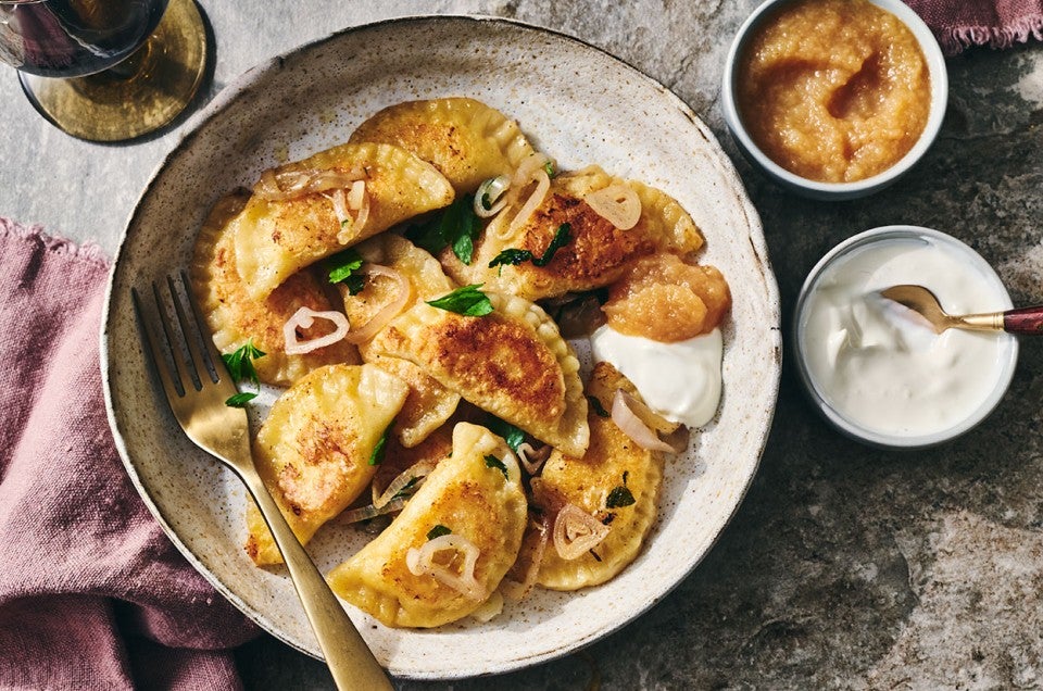 Homemade Pierogis on a plate with perfectly browned exteriors, garnished with herbs and onions. - select to zoom