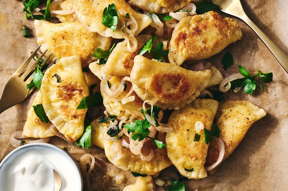 Homemade Pierogis on a plate with perfectly browned exteriors, garnished with herbs and onions. - select to zoom