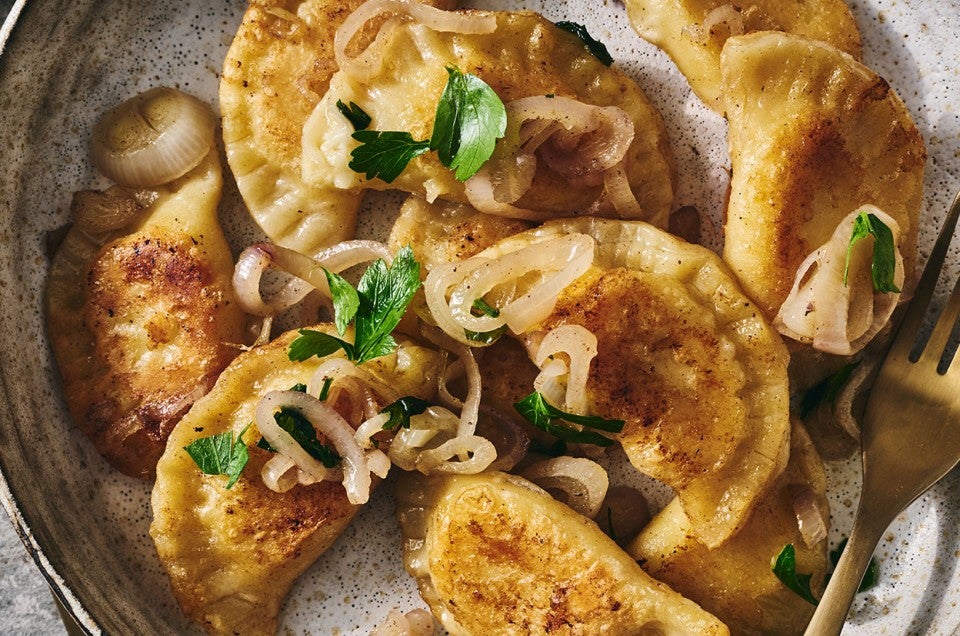 Homemade Pierogis on a plate with perfectly browned exteriors, garnished with herbs and onions. - select to zoom