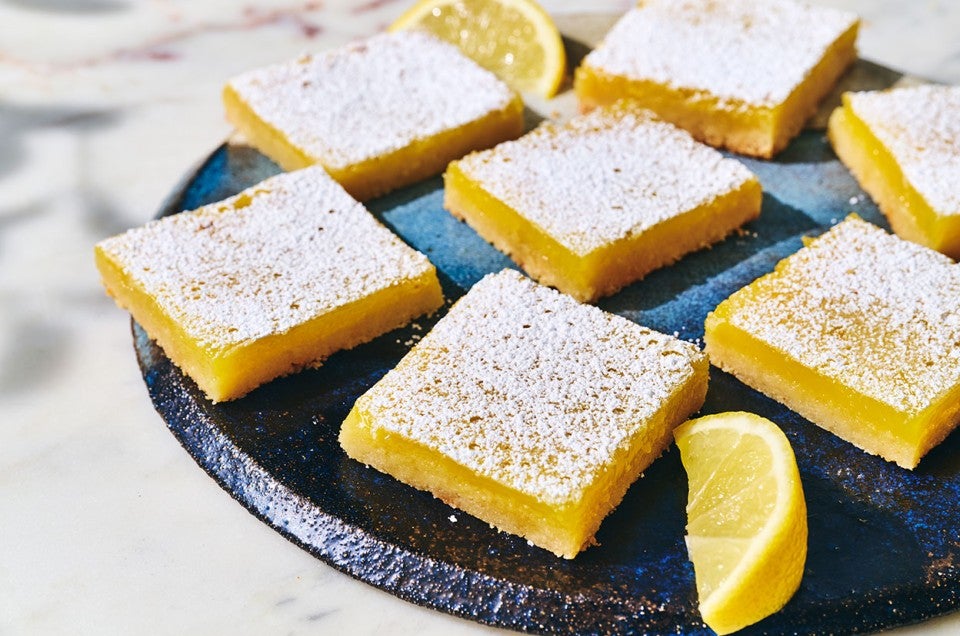 Gluten-Free Lemon Squares with an Almond Flour Crust on a dark plate with a slice of lemon as garnish. - select to zoom