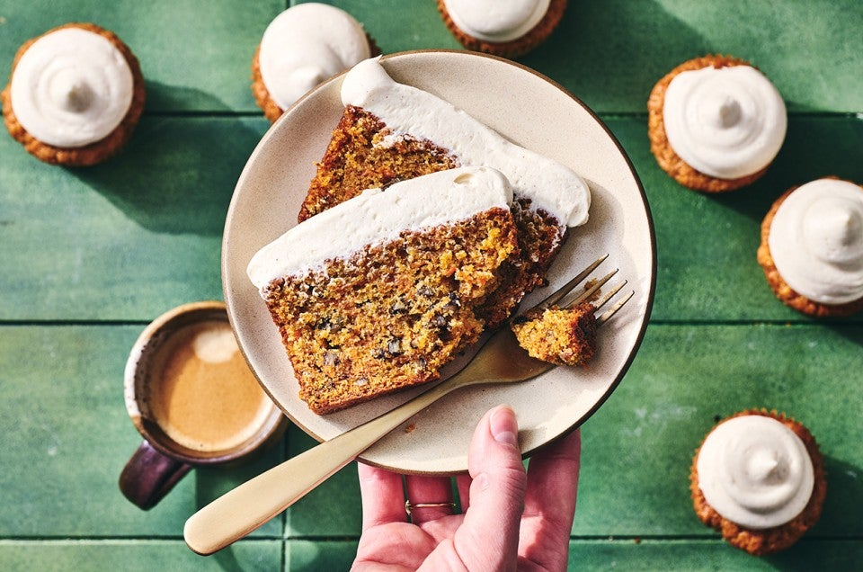 Spiced Carrot Snacking Cake on a plate with a fork and cupcakes in the background. - select to zoom