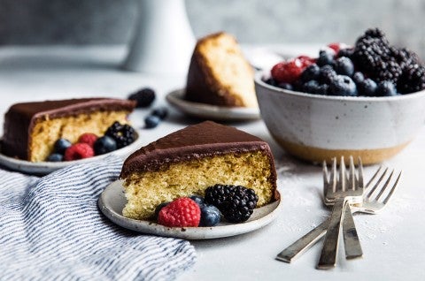 Two slices of yellow cake topped with fudge frosting on plates, garnished with fresh berries - select to zoom