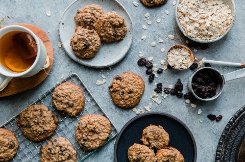 An overhead photo of oatmeal raisin cookies, some rest on a cooling rack while others are shingled together on small plates. The cookies have craggly tops from the oats with puffy centers and golden edges. 