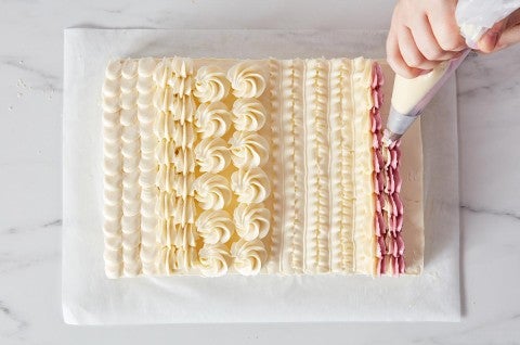 Hands piping designs on a sheet cake