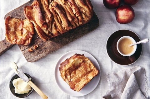 A loaf of Cinnamon Apple Pull-Apart Bread with one slice pulled off, on a plate next to a cup of coffee - select to zoom