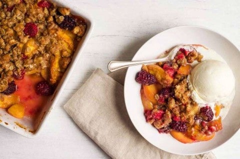 A pan of freshly baked, crumb-topped Summer Fruit Crisp next to a bowl of fruit crisp with a spoon