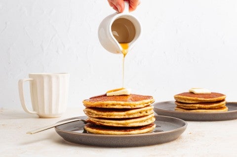 Syrup being poured onto a stack of pancakes