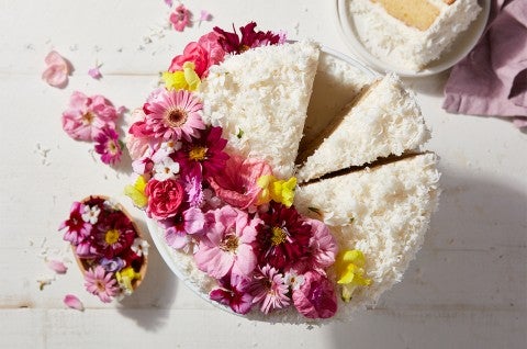 A Old-Fashioned Coconut Cake coated in shredded coconut and decorated with a spray of edible flowers - select to zoom