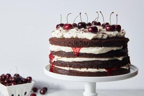 A Black Forest Cake made from layers of chocolate cake and topped with fresh cherries, on a cake stand - select to zoom