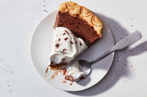 A slice of Chocolate Cream Pie on a plate, topped with whipped cream and chocolate shavings, with a bite on a fork - select to zoom