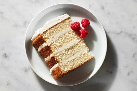 A slice of a four-layer Tender White Cake filled with vanilla buttercream and garnished with raspberries on a plate