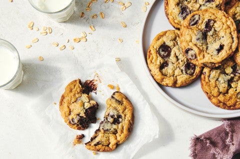 An overhead photo of oatmeal chocolate chip cookies on a plate. One cookie has been put off to the side and broken into pieces showing off the chocolate chips and gooey centers of the cookies. - select to zoom
