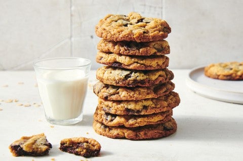 A stack of oatmeal chocolate chip cookies next to a glass of milk. The cookies have crisp golden brown edges and visible chocolate chips. - select to zoom