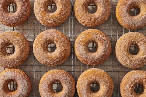 A dozen baked pumpkin donuts on a cooling rack. - select to zoom