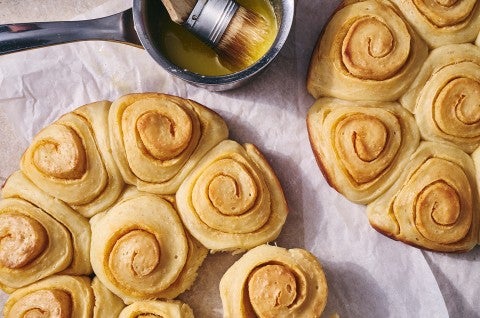 An overhead photo of Buttery Sourdough Buns with a swirl of paprika along side a small pot of melted butter with a pastry brush in it. - select to zoom