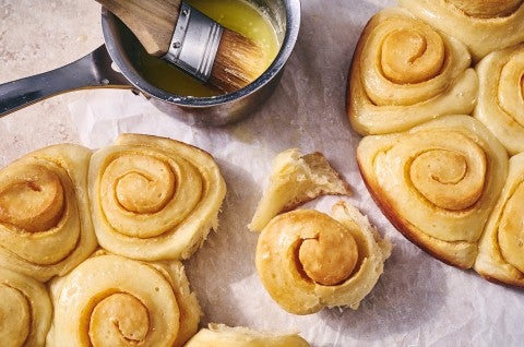 A close up overhead photo of Buttery Sourdough Buns baked close together in rounds pans, one bun has been pulled away to show the soft, flaky interior texture.  - select to zoom