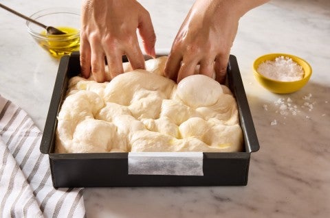 Dimpling focaccia dough in a focaccia pan
