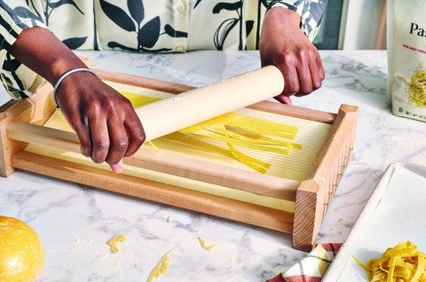 Pasta being pushed through a chitarra pasta cutter