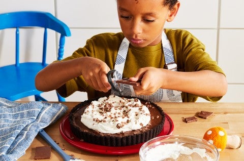 A little boy shaving chocolate onto a pie