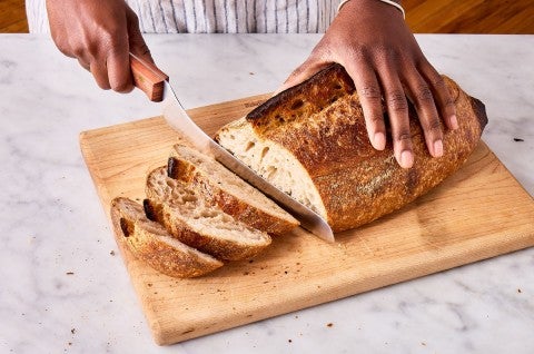 Hands slicing artisan bread loaf with an offset bread knife