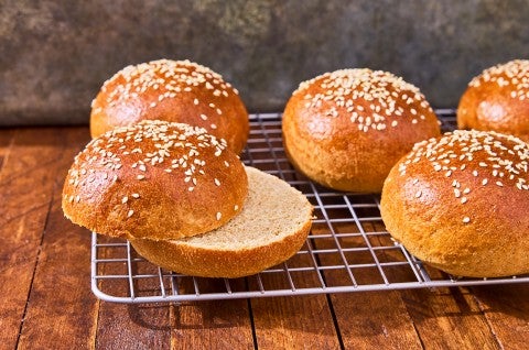 100% Whole Wheat Hamburger Buns on a cooling rack with one sliced - select to zoom