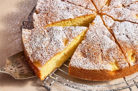 A slice being removed from a Pear and Almond Cake on a cooling rack