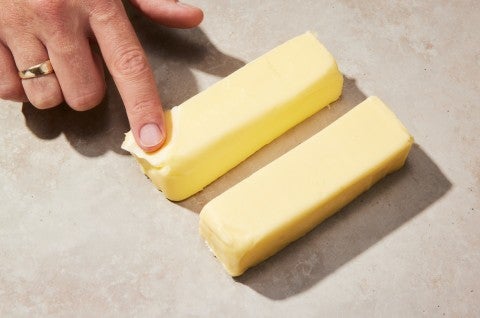 Baker placing their finger on two sticks of cold butter