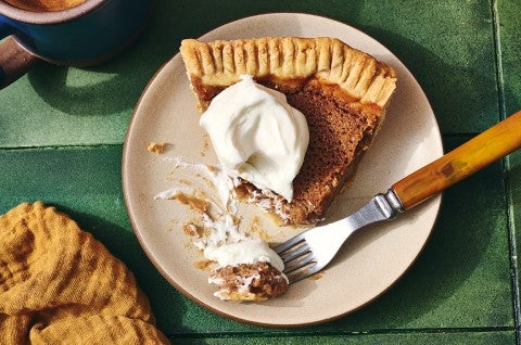 A fork topped with a small bite of apple pie along with the rest of the slice on a plate seen from above.
