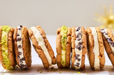 A lineup of cannoli sandwich cookies showing the cookies, a layer of filling, and chocolate chips or pistachio coating. - select to zoom
