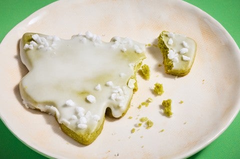 A matcha Christmas tree cookie broken and showing a lovely crumbly green interior on a white plate. - select to zoom