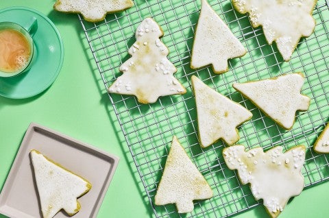 Christmas tree shaped cookies with a light white glaze spread out on a drying rack. - select to zoom