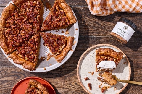 Looking at a rustic table with a pumpkin pecan pie slice and served on a plate, topped with whipped cream. - select to zoom