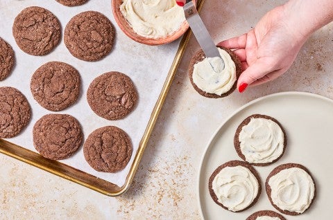 Overhead photograph of hands applying frosting to soft chocolate sugar cookies. - select to zoom