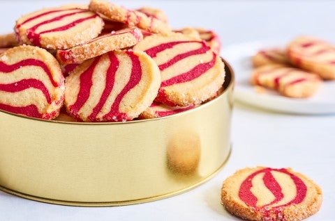 Striped peppermint shortbread cookies inside a gold cookie tin seen from the side. - select to zoom