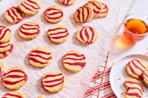 Striped peppermint shortbread cookies laid out on a table with a beverage and plate full of cookies.
