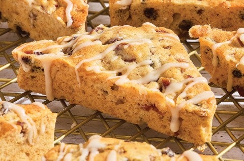 3/4 view of a fruitcake scone showing the glaze drizzled over the top and the edges with a golden brown scone dotted with fruit. - select to zoom