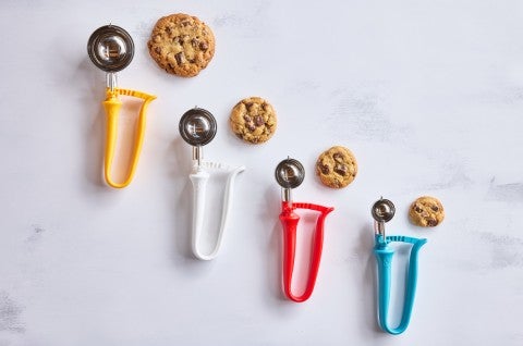 Different sizes of kitchen scoops next to chocolate chip cookies