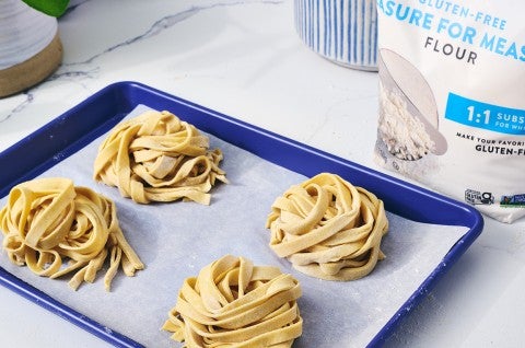 Four balls of raw gluten free pasta sitting on parchment paper on a blue sheet tray. - select to zoom