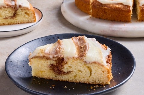 Cinnamon Roll Cake on a dark plate shown from the side with a strong layer of cinnamon and sugar inside the golden cake. - select to zoom