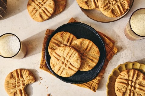 Classic Peanut Butter Cookies spread around a counter layout with some placed on a plate, others on decorative elements, and some on the counter itself. Glasses of milk are present too. - select to zoom