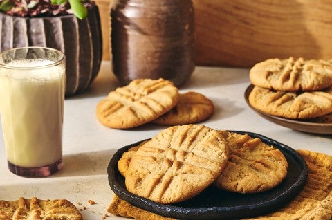 A photograph of Classic Peanut Butter Cookies on a plate with a glass of milk next to it. - select to zoom
