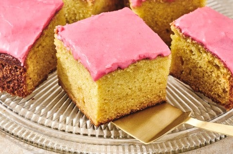 Slices of Cranberry-Orange Olive Oil Cake on a glass plate with golden cake and a pastel pink frosting. - select to zoom