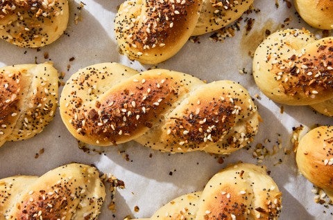 A close up of an Everything Bagel Twist shown fresh out of the oven on parchment with a lovely brown top and bits of everything bagel seasoning. - select to zoom