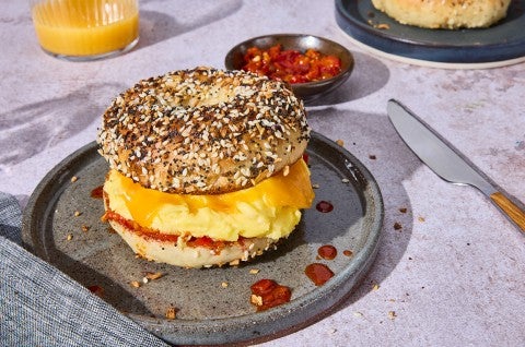 A breakfast sandwich with egg and cheese between a delicious everything bagel on a plate. - select to zoom