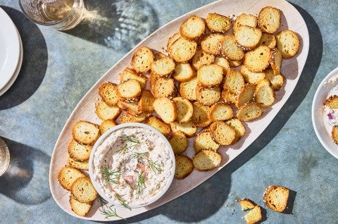 A platter of Everything Bagel Chips spread out around a small bowl of Smoked Salmon Cream Cheese dip. - select to zoom