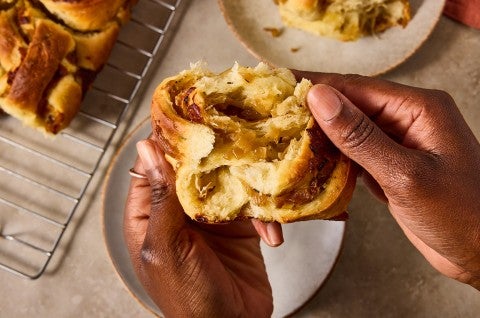 Hands pulling apart a French Onion Roll to show the structure and layers of dough and caramelized onions. - select to zoom